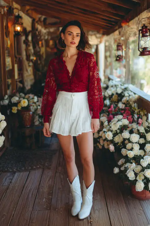 A woman wears a deep red lace long-sleeve top tucked into a white pleated mini skirt with white cowboy boots