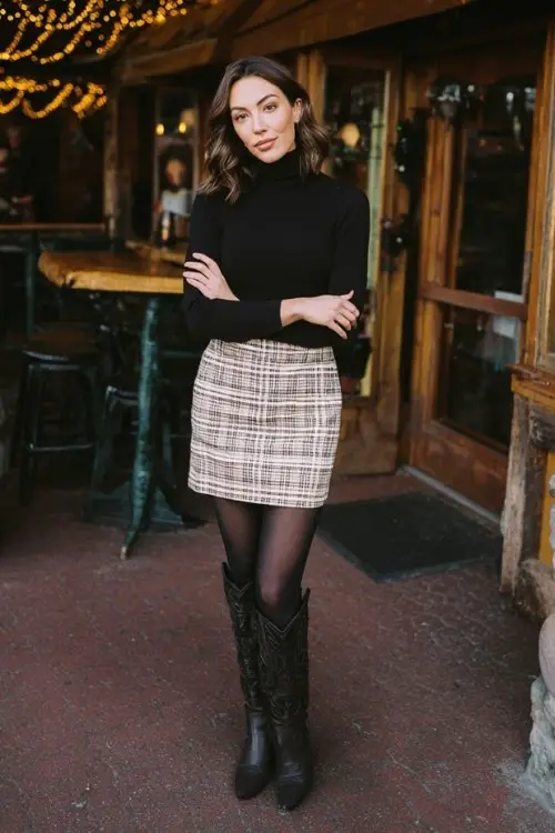 A woman wears a plaid wool mini skirt with black tights, a fitted turtleneck, and tall black cowboy boots