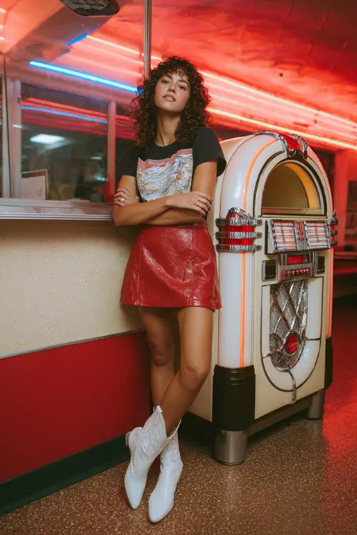 A woman wears a red leather mini skirt with a black graphic tee and white cowboy boots