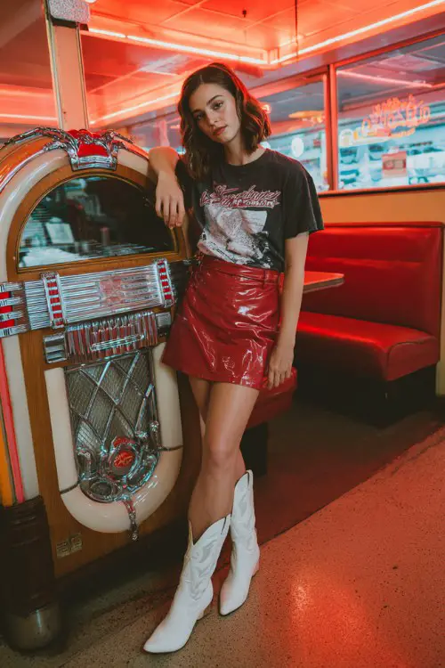 A woman wears a red leather mini skirt with a black graphic tee and white cowboy boots
