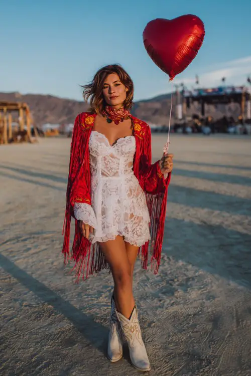 A woman wears a white lace mini dress with a red fringe shawl and embroidered cowboy boots