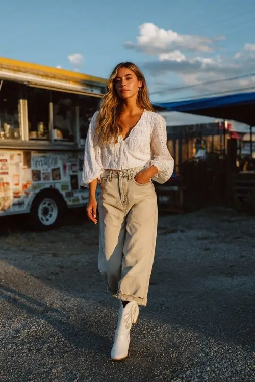 A woman wears distressed jeans, a flowy white blouse, and white cowboy boots