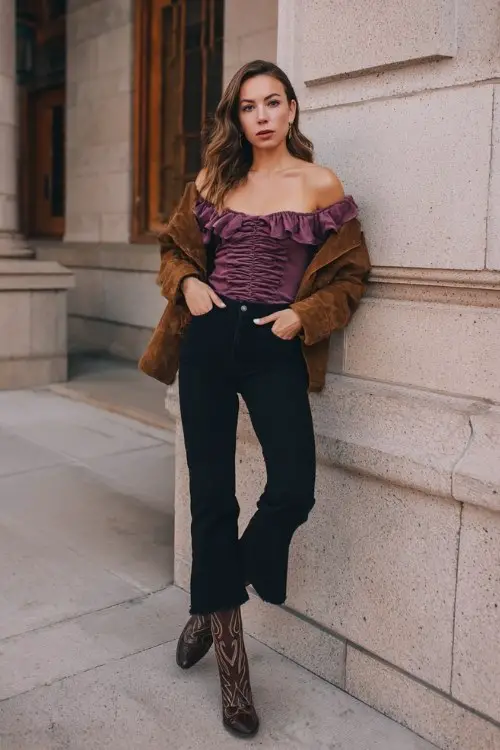 A woman wears high-waisted black jeans paired with a ruched off-shoulder top in plum, layered under a cropped suede jacket and styled with classic western boots (2)