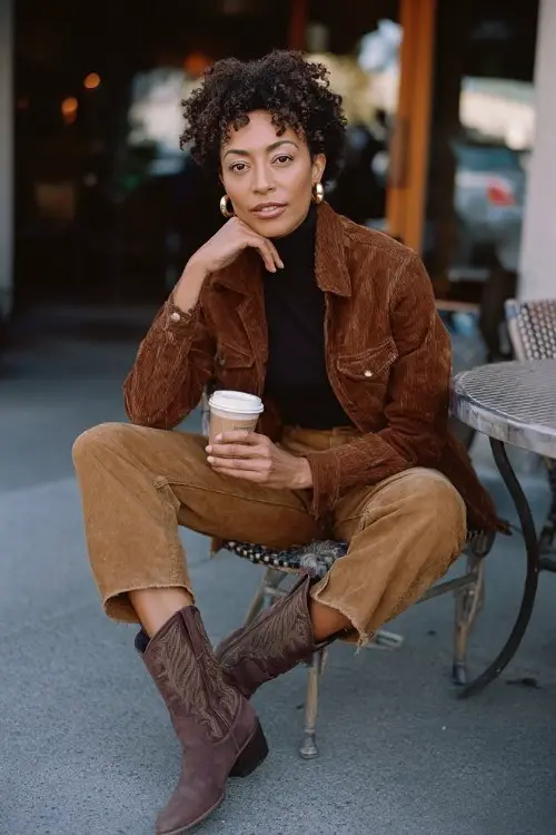A woman wears straight-leg jeans, a fitted turtleneck, a suede jacket, and chocolate brown cowboy boots