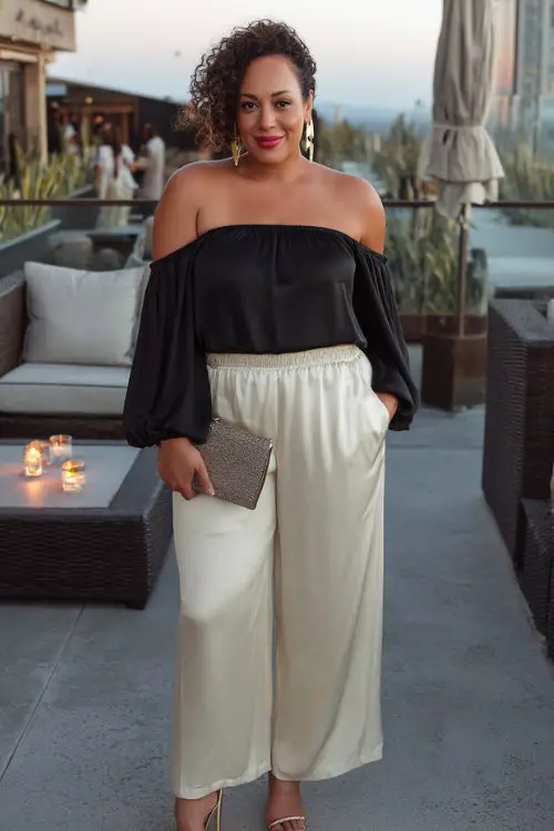 A curvy woman wears a silky off-the-shoulder top with wide-leg trousers and strappy heels, accessorized with a sleek clutch and gold hoops for a rooftop lounge first date