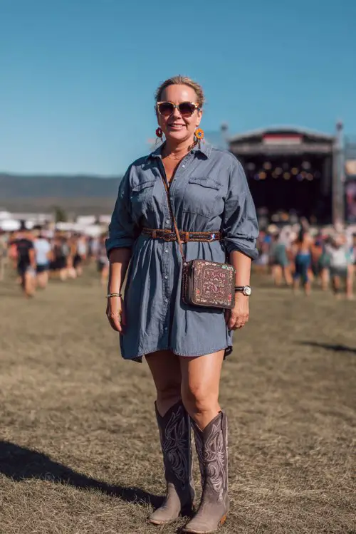 A full body plus-size woman over 40 wears a denim shirt dress paired with embroidered cowboy boots, statement earrings