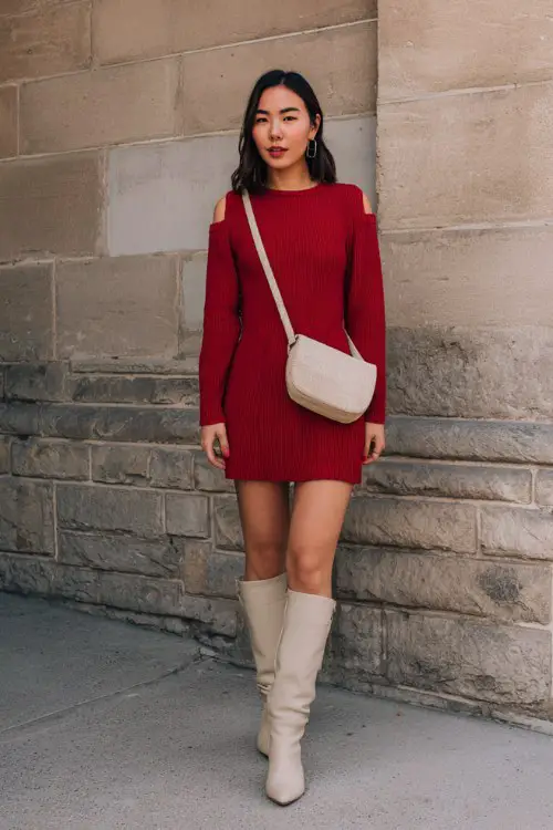 A petite woman wears a cherry-red ribbed knit dress with knee-high boots and a neutral crossbody bag