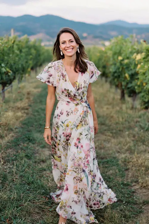 A stylish woman in her 50s wears a floor-length floral print chiffon gown with flutter sleeves