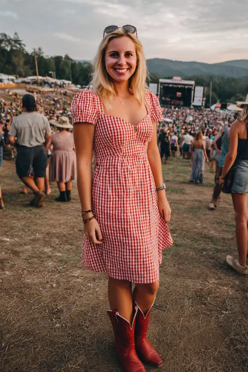 A woman over 30 wears a red and white checked midi dress with a fitted waist and red cowgirl boots at a concert