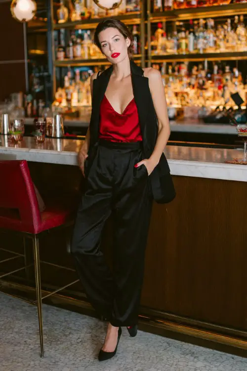 A woman over 40 wears a tailored black pantsuit with a silk red camisole underneath, red lipstick, and stiletto heels