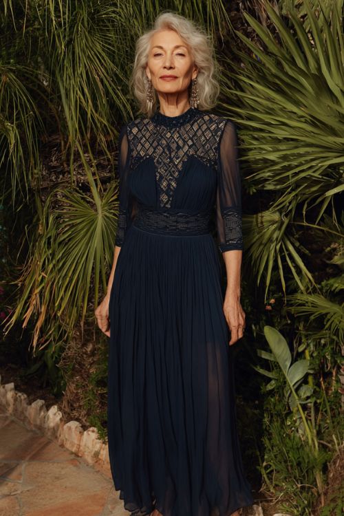 A woman over 50 wears a navy gown with a pleated bodice and semi-sheer three-quarter sleeves featuring tonal geometric embroidery