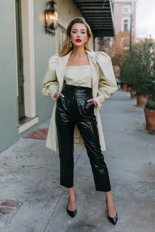 A woman styles a square-neck puff sleeve top with faux leather pants and pumps, topped with a trench coat and bold lipstick