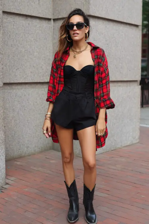 A woman wears high-waisted shorts styled with black cowboy boots, a structured bustier top and oversized plaid shirt worn open