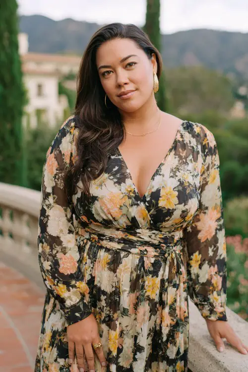 Sophisticated plus size woman in flowy floral spring wedding guest dress, flattering silhouette, outdoor wedding backdrop