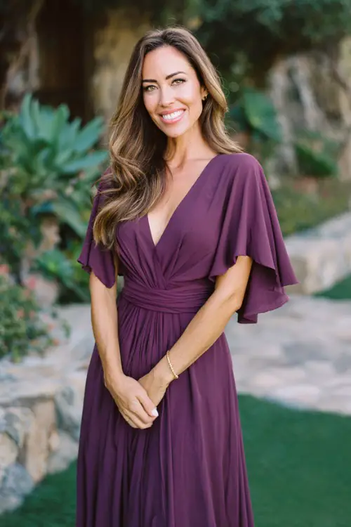 Timeless classy spring wedding guest fashion, woman over 40, plum purple flowing maxi dress with cape sleeves
