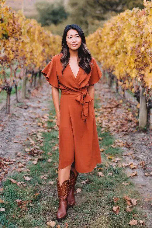 a woman in a rust-colored wrap midi dress with flutter sleeves and a waist tie, paired with classic brown cowboy boots