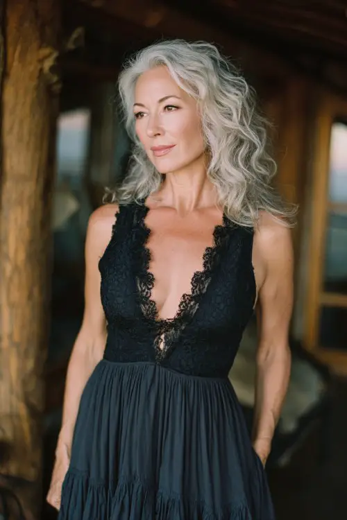 petite woman over 50 wearing a dark color flowy maxi dress with lace bodice and deep v-neckline, sleeveless, soft layered skirt with movement