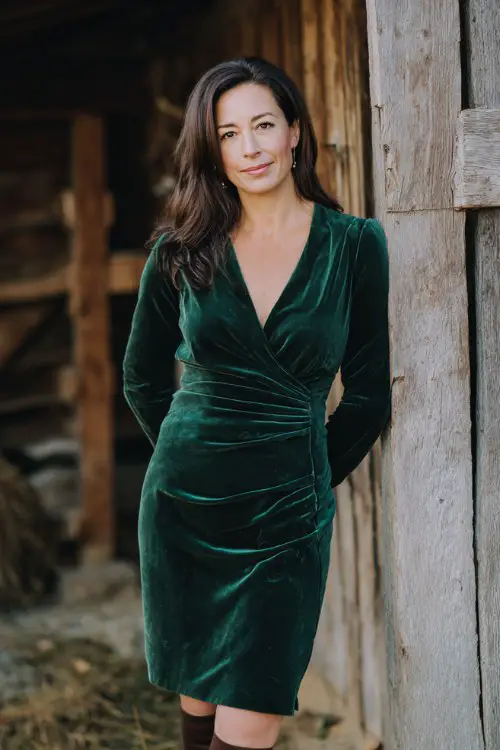 petite woman over 50 wearing a deep green velvet long-sleeve dress with v-neckline, knee-length, paired with heeled boots