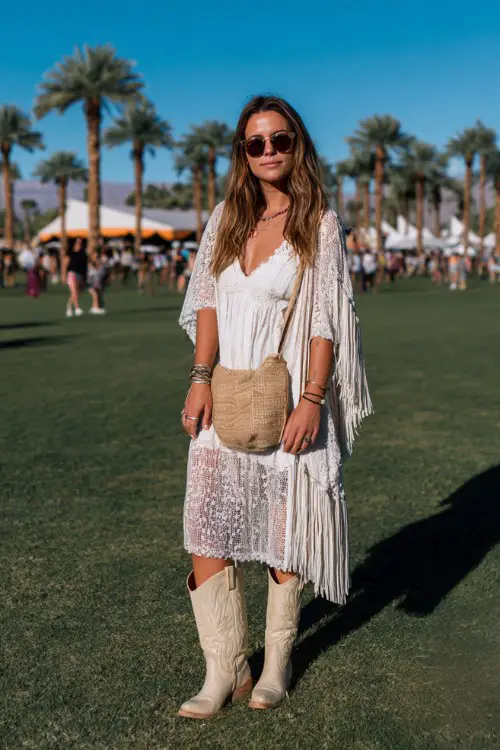 A curvy white woman wears cream cowboy boots with a lace-trim midi dress and lightweight kimono, styled with chunky rings and a fringe bag