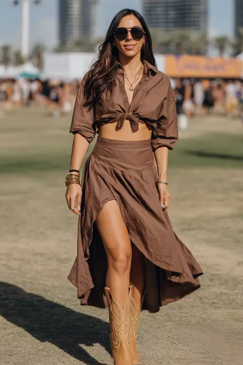 A curvy white woman wears tan cowboy boots with a chic monochrome two-piece set featuring a cropped blouse and flowy skirt, styled with stacked bracelets and bold sunglasses