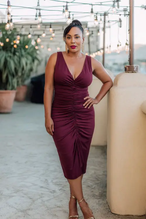 A curvy woman over 40 wears a burgundy mermaid midi dress with subtle ruching and ankle-strap heels
