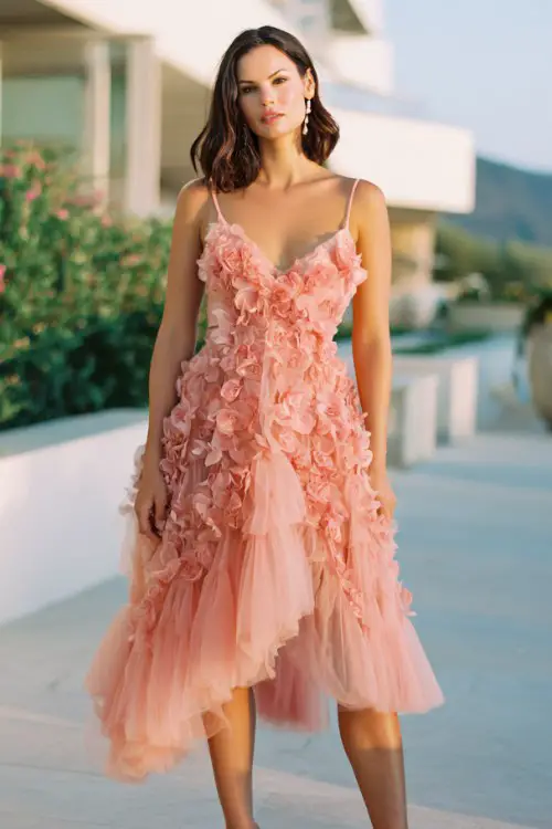 A curvy woman wears a breezy coral tulle midi dress with delicate 3D floral appliqué and layered skirt movement, styled with elegant heeled sandals