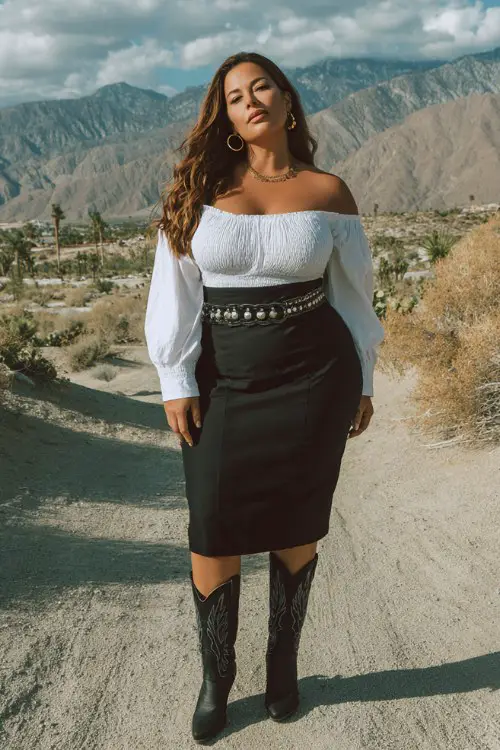 A curvy woman wears black cowboy boots with a structured midi skirt and elegant off-shoulder blouse, accessorized with a wide statement belt and hoop earrings