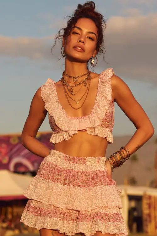 A fashionable woman wearing a ruffled sleeveless crop top with layered tiers and a deep V neckline, paired with a matching high-waisted mini skirt with soft ruffles and a small floral pattern