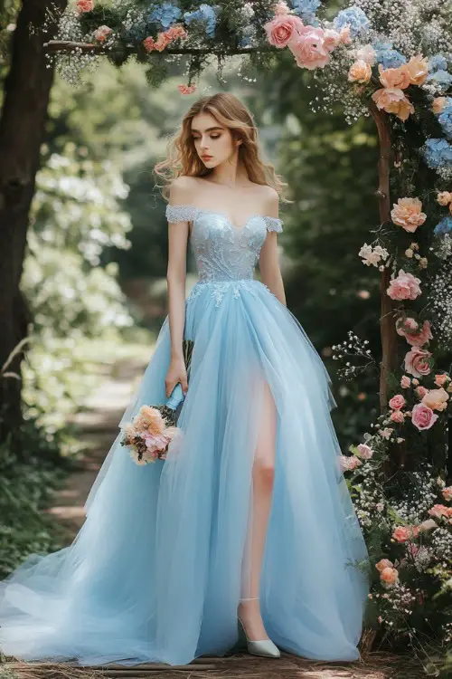 A woman in a light blue knee-length dress with a fitted lace bodice and a voluminous tulle skirt, standing beside a floral arch at a spring garden wedding