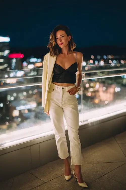 A woman over 30 wears high-waisted dark wash straight-leg jeans with a silky black camisole, styled with pointed-toe heels and a cropped blazer