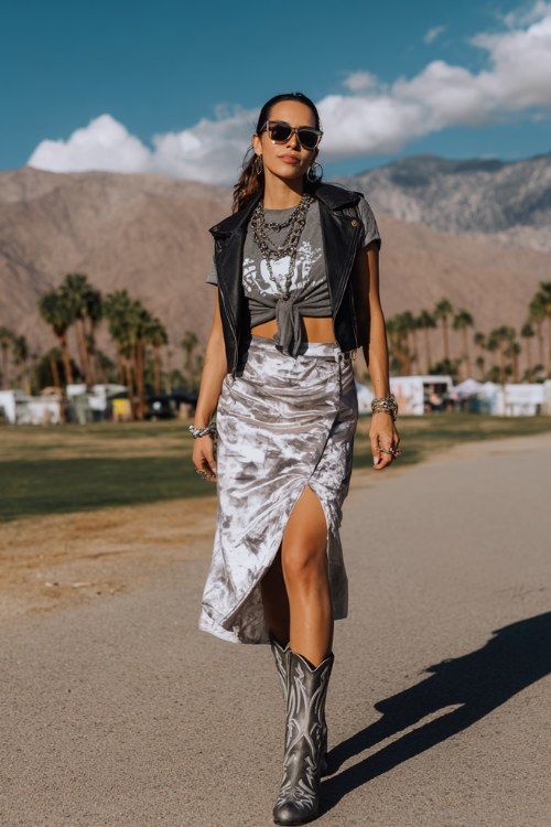 A woman over 30 wears silver cowboy boots with a silky slip skirt and fitted graphic tee knotted at the waist