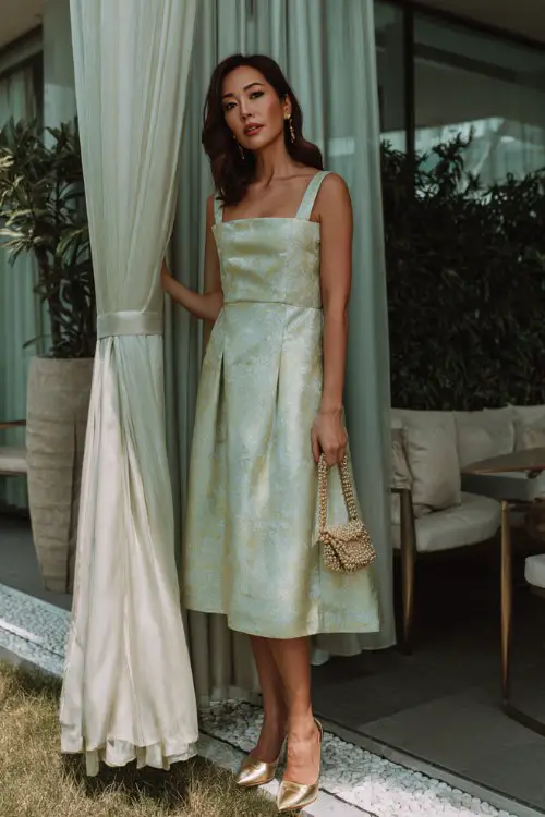 A woman over 40 wears a pale green jacquard A-line dress with a square neckline and thick straps