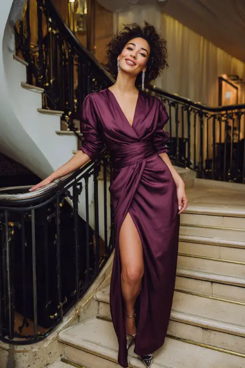 A woman over 40 wears a rich plum wrap-effect gown with an asymmetric neckline and satin texture, paired with chrome heels