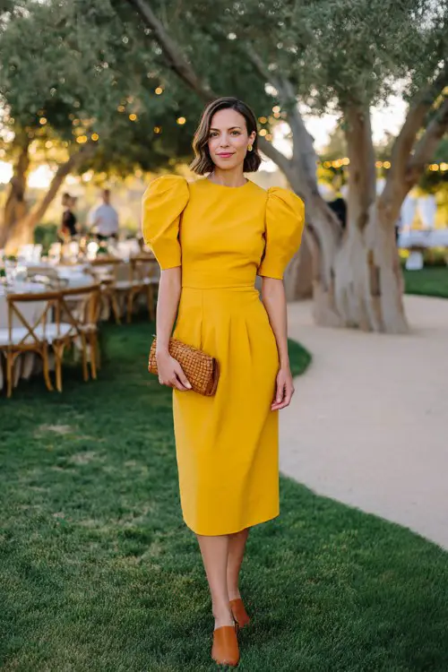 A woman over 40 wears a saffron yellow midi dress with architectural puff sleeves and a defined waist seam (2)
