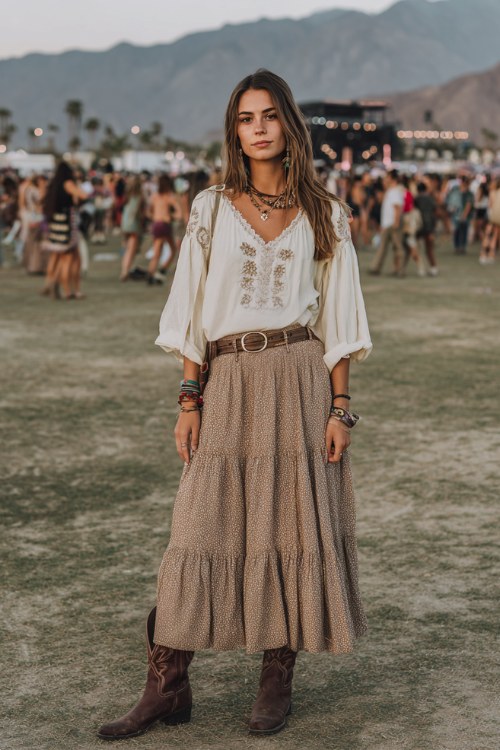 A woman wearing a modest boho festival outfit with a loose embroidered blouse tucked into a tiered maxi skirt, belt and classic cowboy boots