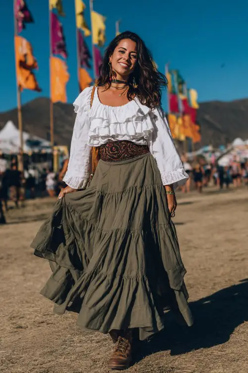 A woman wearing a modest boho festival outfit with a white ruffled peasant blouse and a flowy olive green tiered maxi skirt, wide boho belt at the waist, lace-up boots