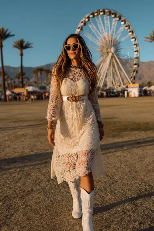 A woman wearing a modest lace midi dress with long sleeves styled with white cowboy boots and a western belt, layered jewelry and oversized sunglasses