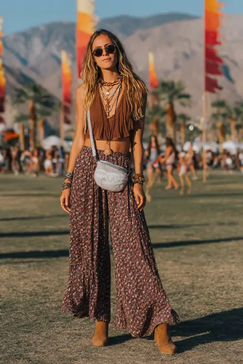 A woman wearing modest boho wide leg patterned pants with a loose peasant blouse and layered necklaces, suede ankle boots and crossbody bag
