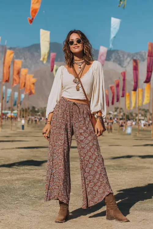 A woman wearing modest boho wide leg patterned pants with a loose peasant blouse and layered necklaces, suede ankle boots and crossbody bag