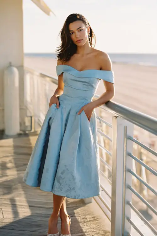 A woman wears a sophisticated off-shoulder satin midi dress in pale blue with subtle floral jacquard texture
