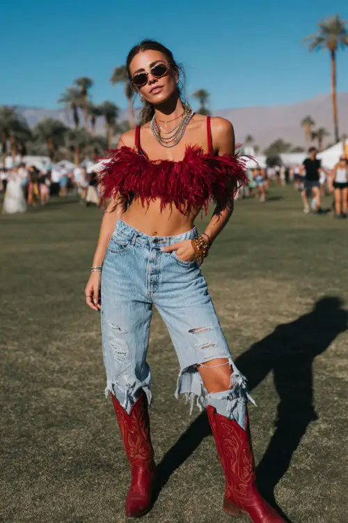 A woman wears red cowboy boots with high-rise ripped jeans and a dramatic feather-trimmed crop top
