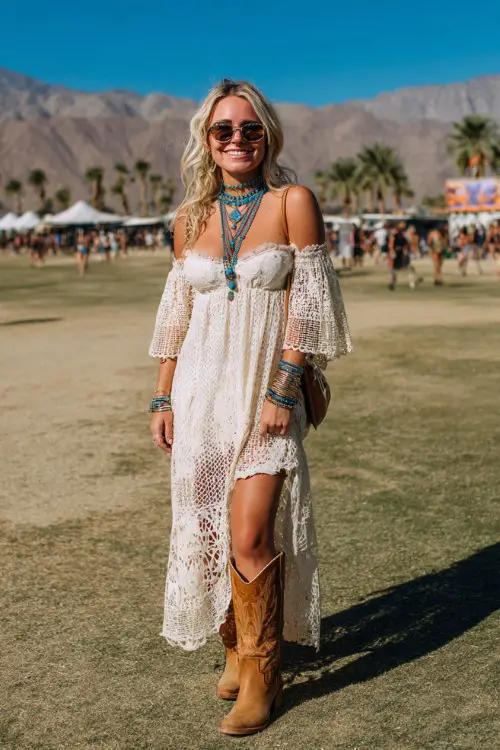 A woman wears tan cowboy boots with a flowy crochet maxi dress featuring bell sleeves and intricate lace details, styled with layered turquoise necklaces and stacked bangles