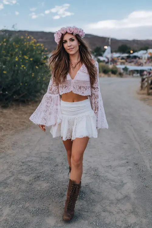 Coachella-inspired boho outfit with soft pink rose flower crown, white lace crop top and matching lace mini skirt, flared lace sleeves, brown lace-up combat boots, tousled long hair