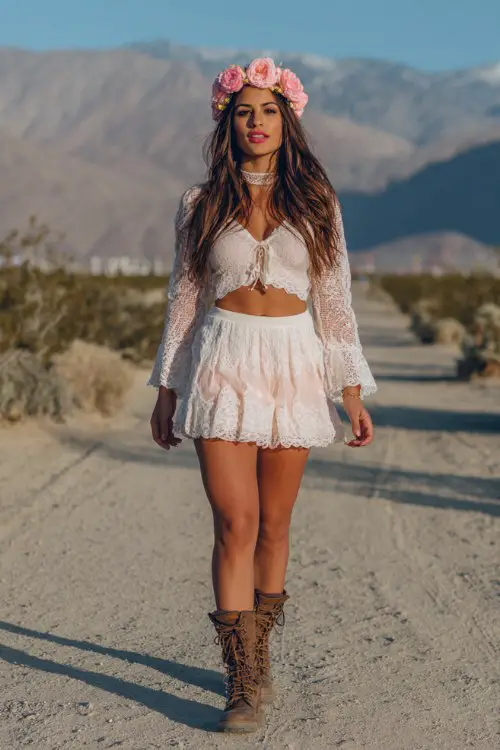 Coachella-inspired boho outfit with soft pink rose flower crown, white lace crop top and matching lace mini skirt, flared lace sleeves, brown lace-up combat boots