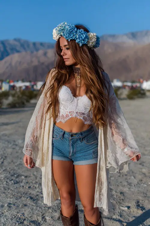 Coachella sunset look featuring a blue hydrangea flower crown, white lace corset top, vintage high-waisted denim shorts, sheer oversized kimono flowing in the wind
