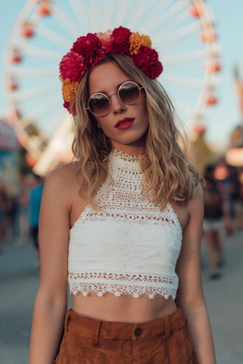 Festival look featuring crochet crop top and high-waisted suede shorts, bold red and pink flower crown, round sunglasses