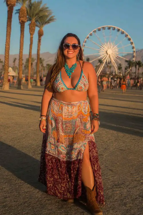 Plus-size white woman at a desert music festival, wearing a colorful crochet bralette and high-waisted flowy maxi skirt with slit, layered turquoise jewelry