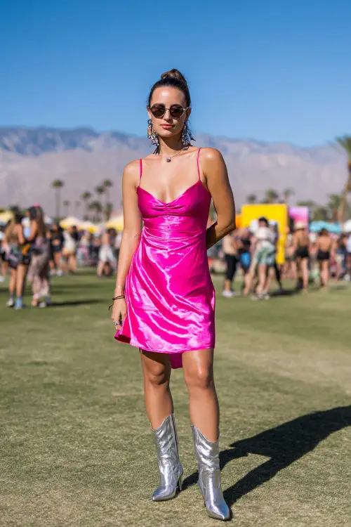 Woman in a bright pink satin slip dress, silver boots, statement earrings, slicked-back bun