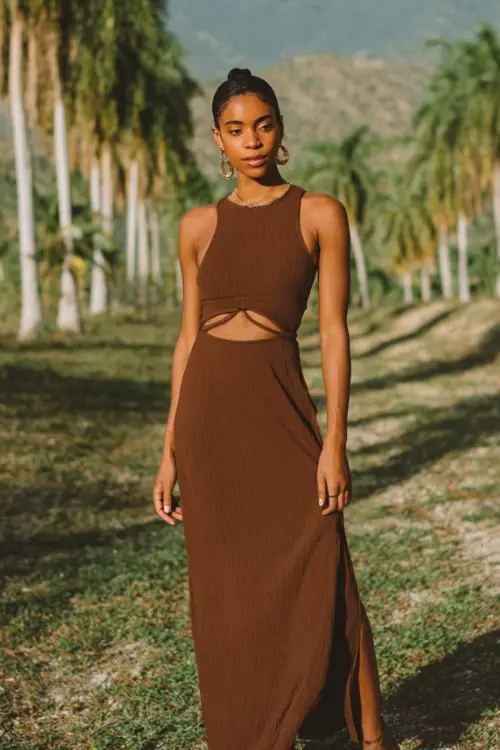 Woman in a brown cut-out knit maxi dress, leather sandals, minimal gold jewelry, sleek low bun