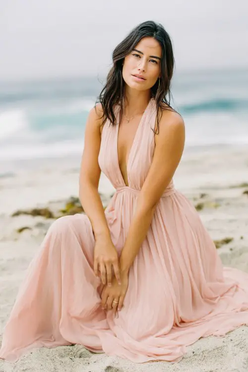 a woman wears a flowy blush pink wedding guest dress at a beach wedding